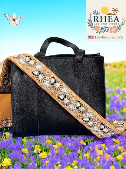 Rhea Artistry Studio 2-inch wide crossbody strap with embroidered trillium flowers in beige, black, and silver, featuring brushed brass hardware.