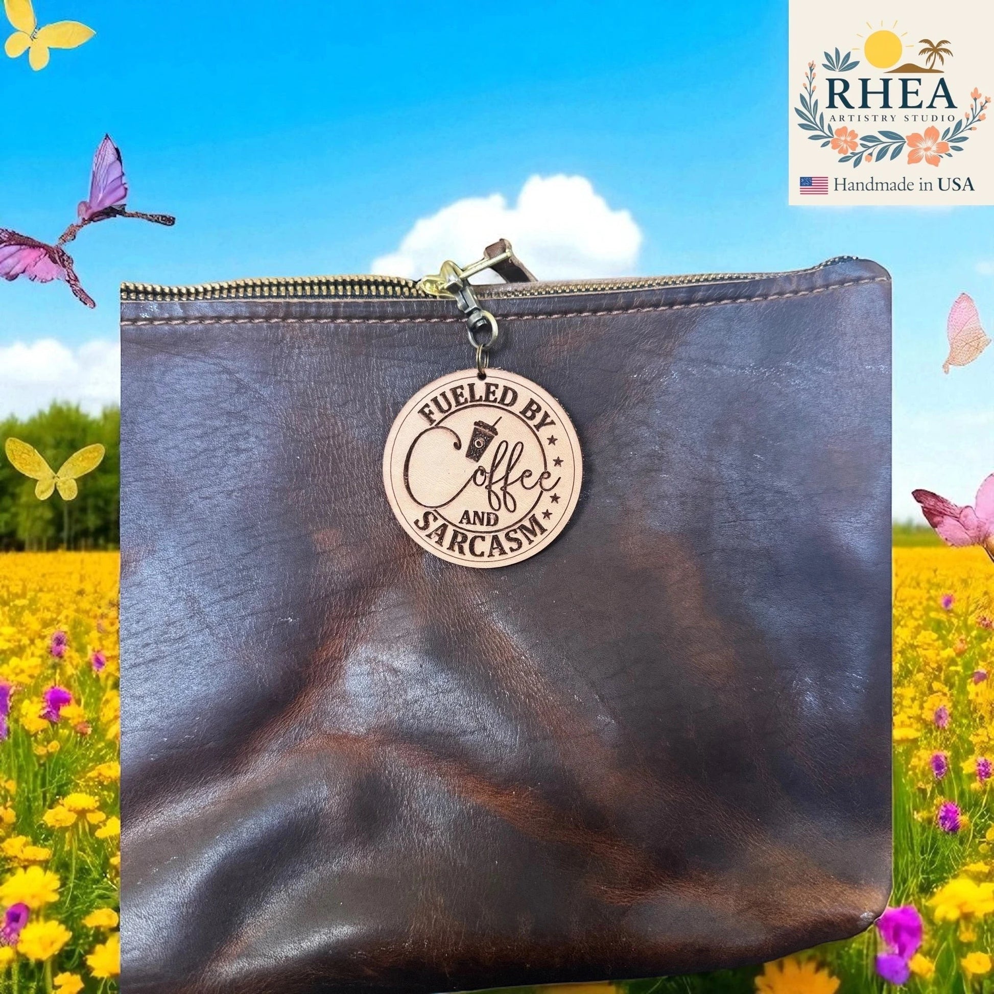 Rhea Artistry Studio engraved leather tag with "Fueled by Coffee and Sarcasm" text and coffee cup graphic, attached to a dark brown leather bag.
