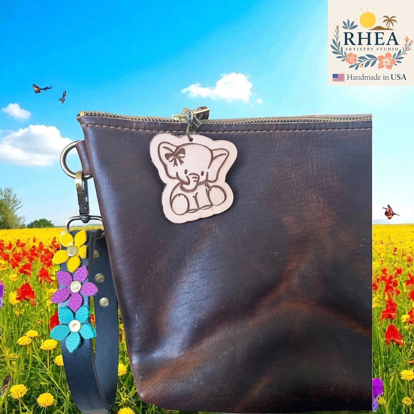 Rhea Artistry Studio natural leather tag engraved with a cute elephant wearing a bow, attached to a dark brown leather bag.