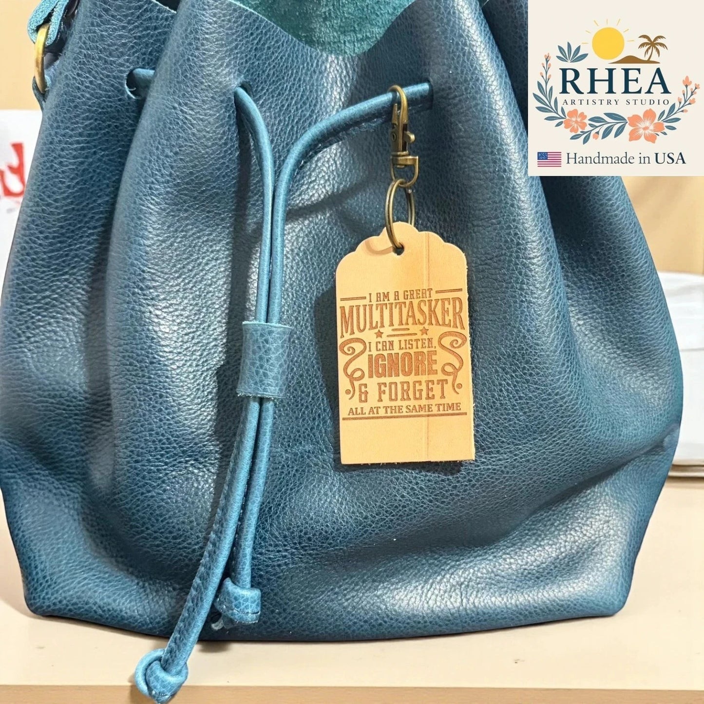 Rhea Artistry Studio engraved leather tag with witty quote on a blue leather drawstring bag.