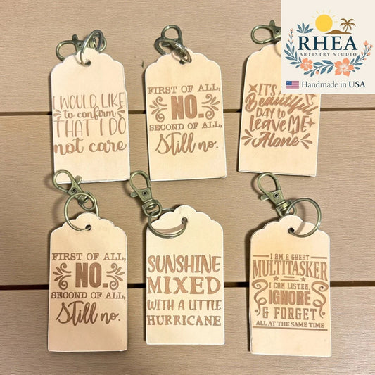 Rhea Artistry Studio collection of six natural vegetable-tanned leather tags with engraved witty quotes and antique brass keychain clips.