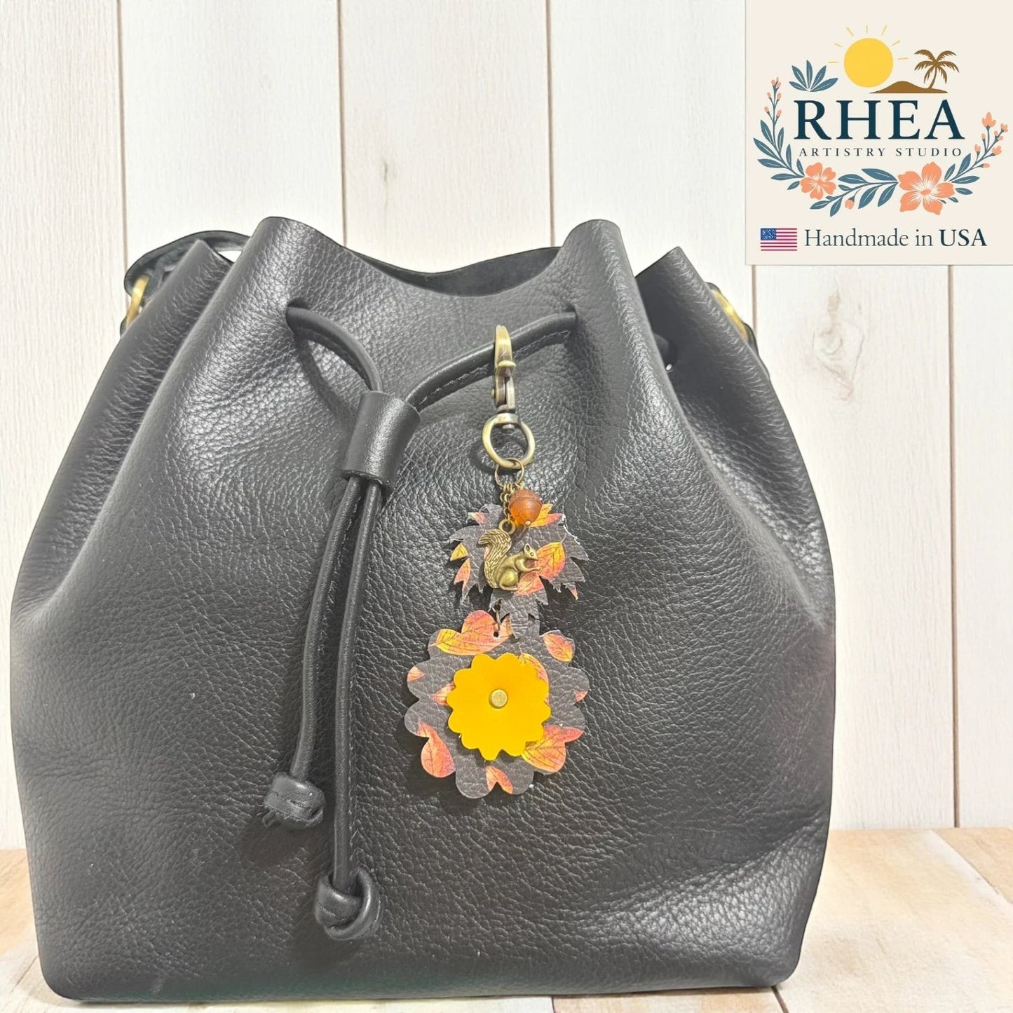 Rhea Artistry Studio fall leather charm with acorn and squirrel silhouette, autumn leaves, and yellow flower detail. Perfect as a bag accessory or keychain.