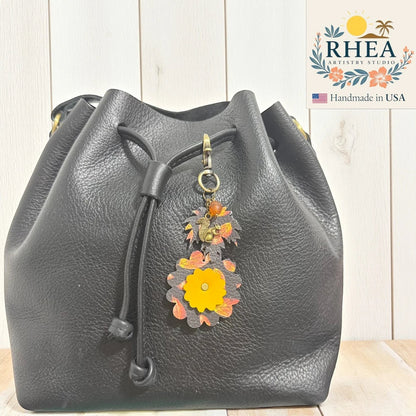 Rhea Artistry Studio fall leather charm with acorn and squirrel silhouette, autumn leaves, and yellow flower detail. Perfect as a bag accessory or keychain.