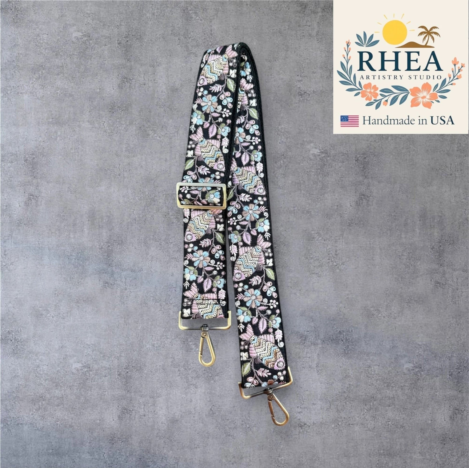 Rhea Artistry Studio 2-inch wide crossbody strap with black background and colorful embroidered fish and floral pattern. Adjustable with brushed brass hardware.