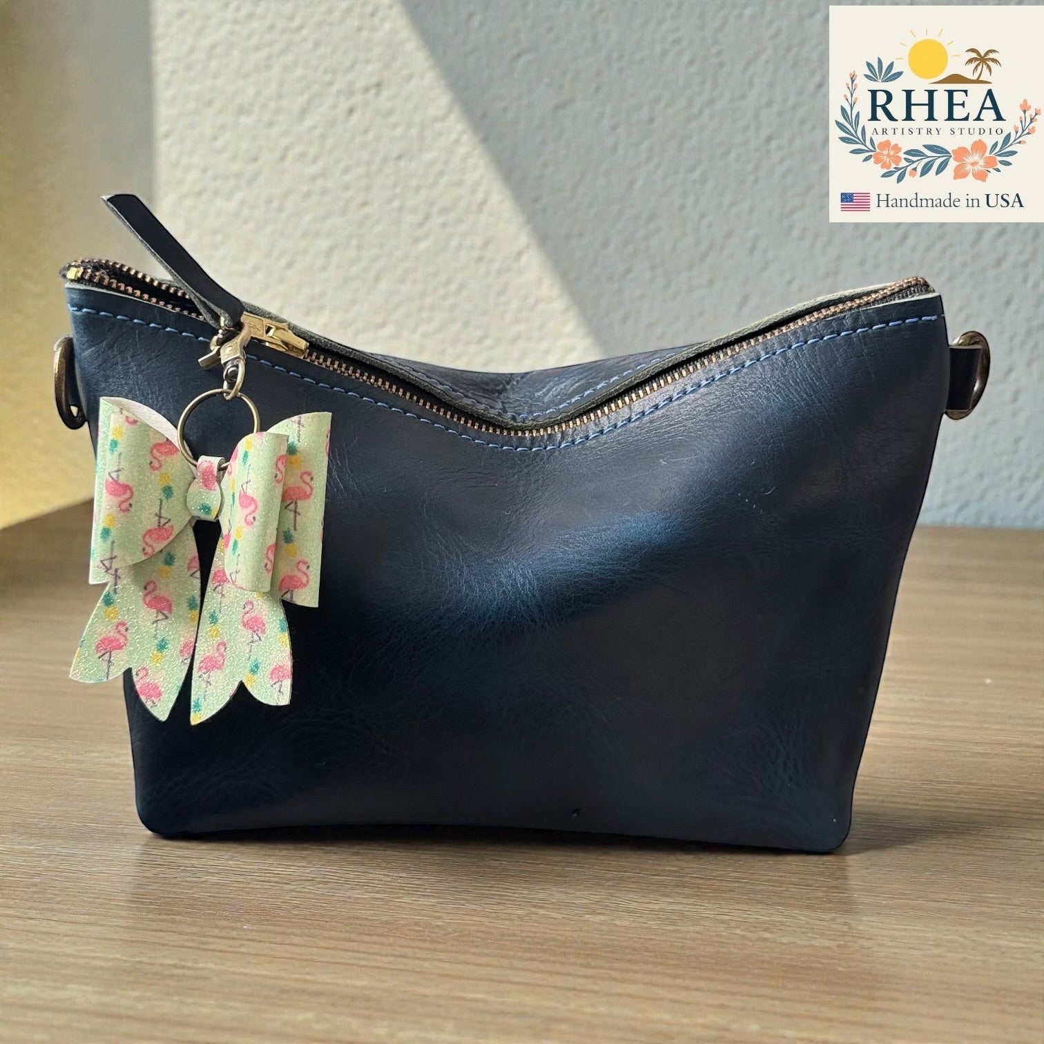Rhea Artistry Studio handmade double-layer French bow charm with flamingo print and brass hardware, clipped to a navy blue leather bag.