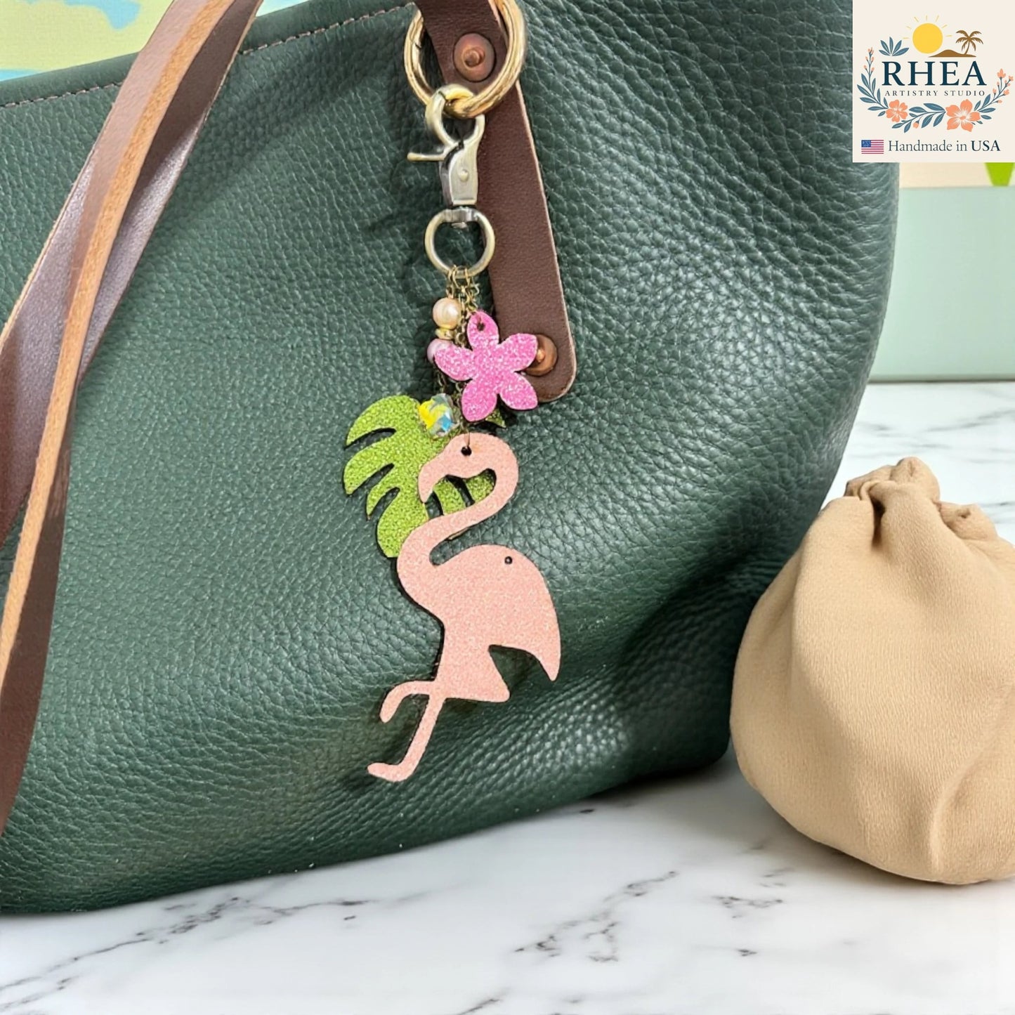 Rhea Artistry Studio pink glitter leather flamingo charm with tropical leaf, pink flower, pearls, and gemstone beads on antique brass hardware.