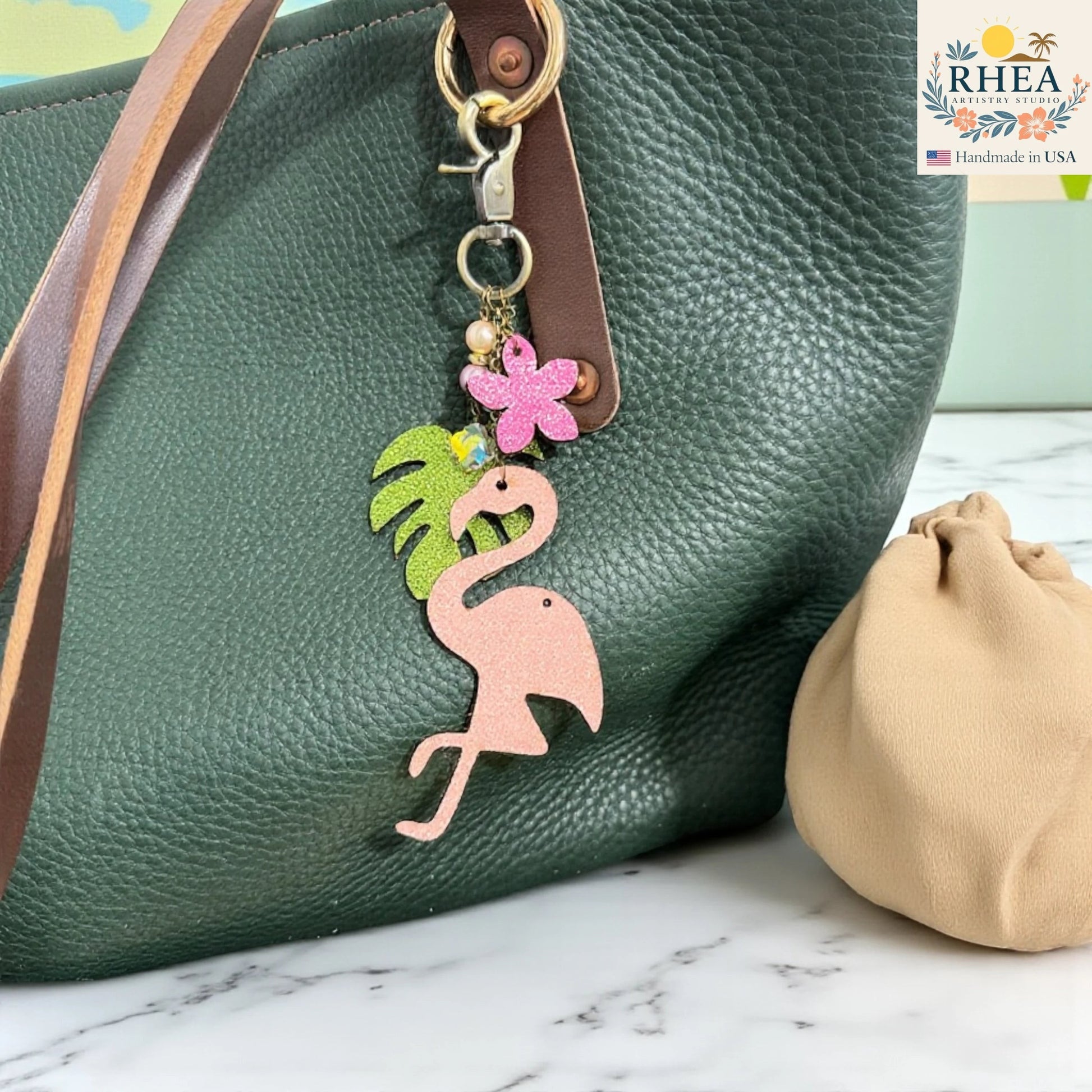 Rhea Artistry Studio pink glitter leather flamingo charm with tropical leaf, pink flower, pearls, and gemstone beads on antique brass hardware.