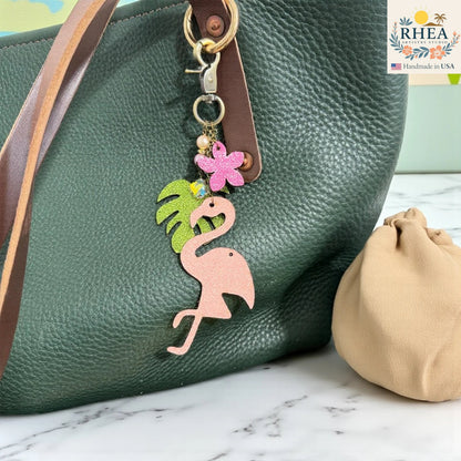 Rhea Artistry Studio pink glitter leather flamingo charm with tropical leaf, pink flower, pearls, and gemstone beads on antique brass hardware.