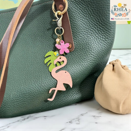 Rhea Artistry Studio pink glitter leather flamingo charm with tropical leaf, pink flower, pearls, and gemstone beads on antique brass hardware.