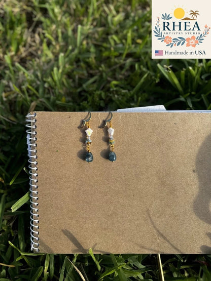 Rhea Artistry Studio white and silver floral glass drop earrings with blue gemstone and 24k gold-plated brass lever-back closures.