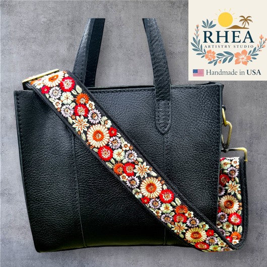 Rhea Artistry Studio black leather tote with a 2-inch wide adjustable strap featuring colorful floral embroidery in red, orange, and white.