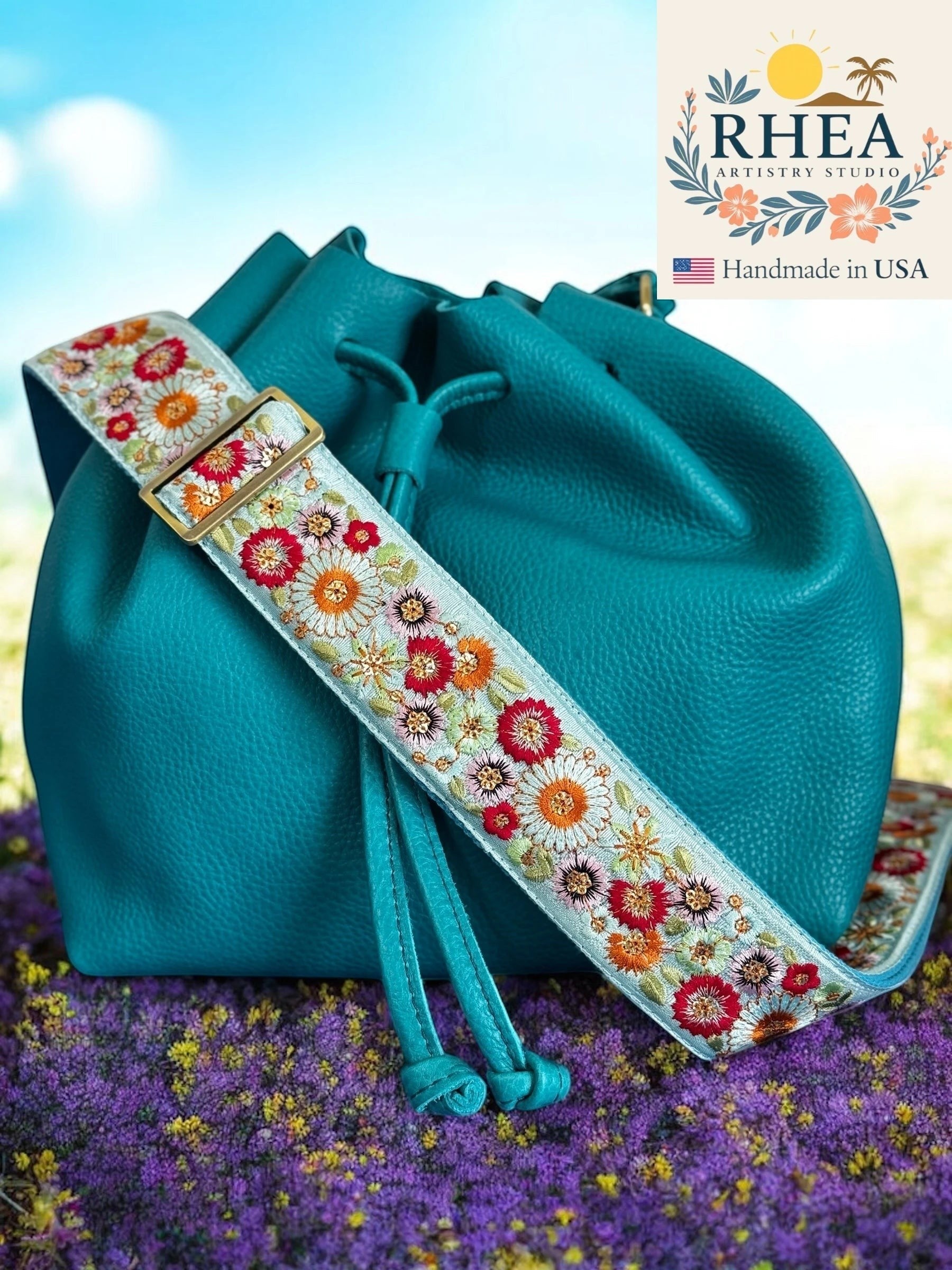 Rhea Artistry Studio 2-inch wide adjustable strap with colorful floral embroidery and brushed brass hardware, shown on a teal bucket bag.