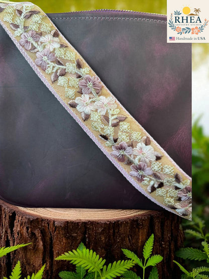Rhea Artistry Studio 1.5-inch crossbody strap with yellow and pink floral embroidery on a tan background, adjustable length, and brass hardware.