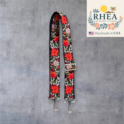 Rhea Artistry Studio black crossbody strap with vibrant red and pink floral embroidery, 1.5-inch width, adjustable length, brushed brass hardware.