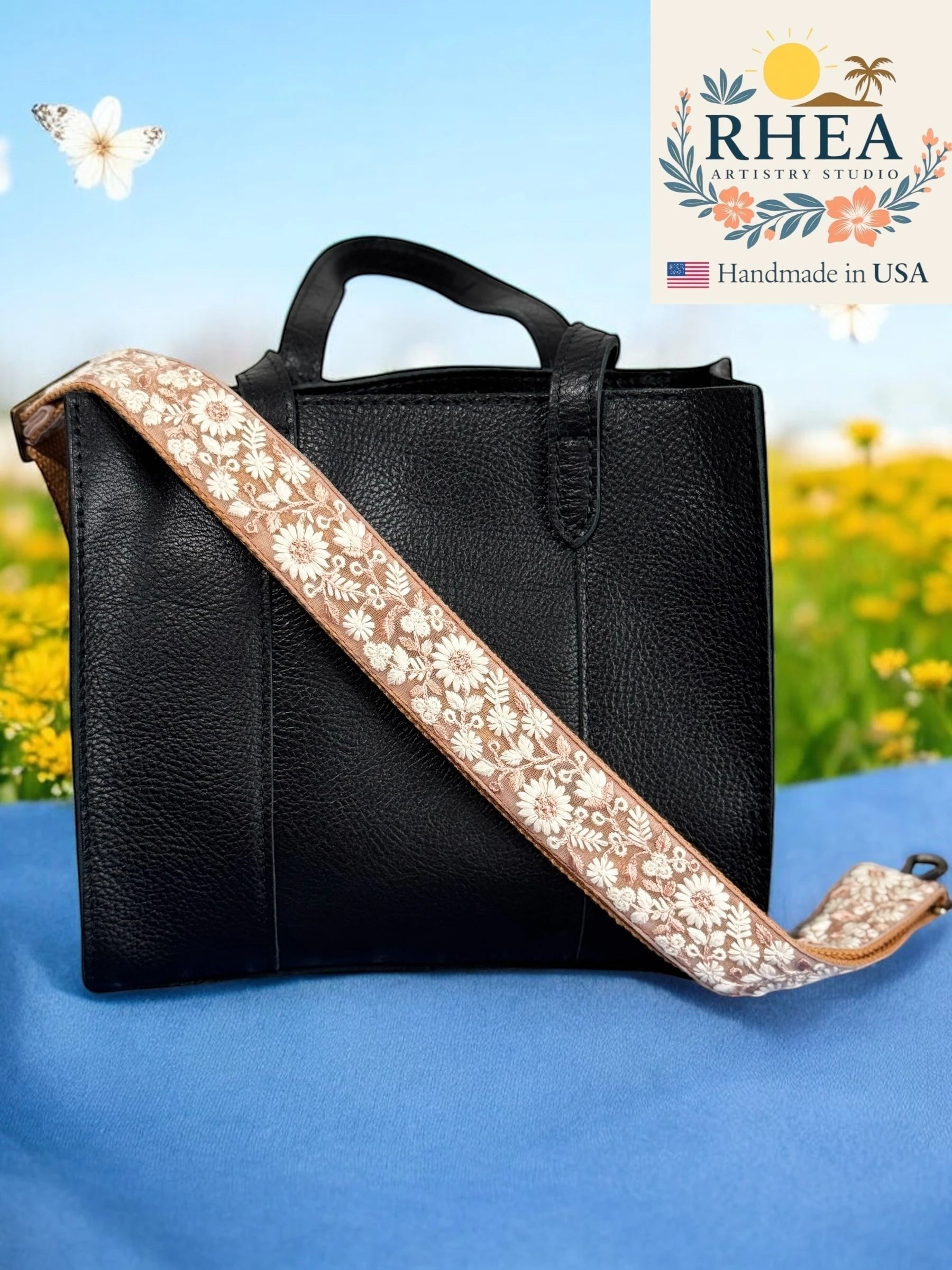 Rhea Artistry Studio tan crossbody strap with white floral embroidery, adjustable length, and brushed brass hardware.