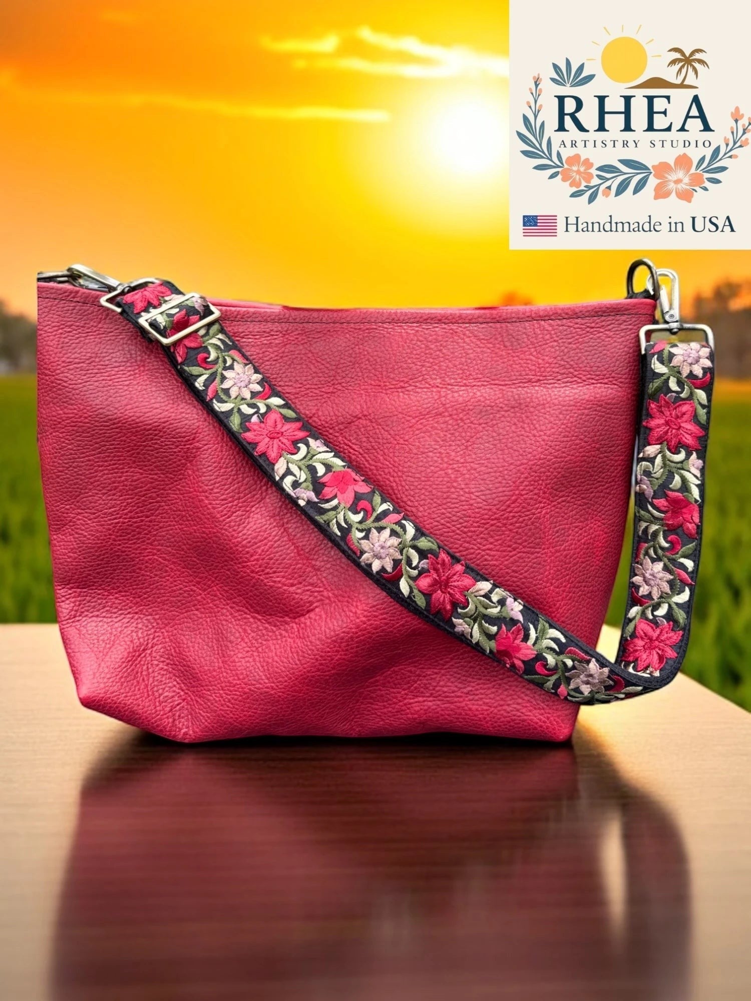 Rhea Artistry Studio 1.5-inch crossbody strap with vibrant floral embroidery in pink and green on black webbing, featuring brushed brass hardware.