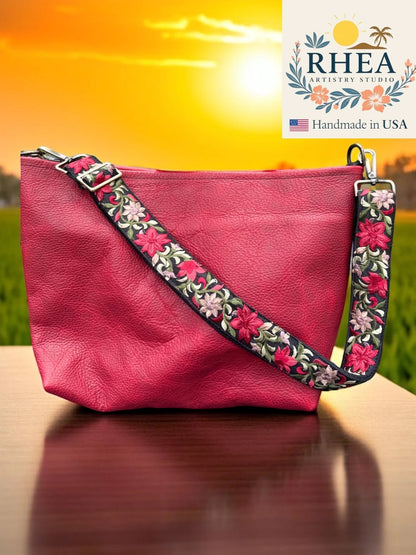 Rhea Artistry Studio 1.5-inch crossbody strap with vibrant floral embroidery in pink and green on black webbing, featuring brushed brass hardware.