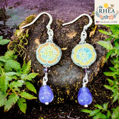 Rhea Artistry Studio Iris Glow Czech floral glass bead drop earrings with faceted purple gemstone teardrops and crystal accents.