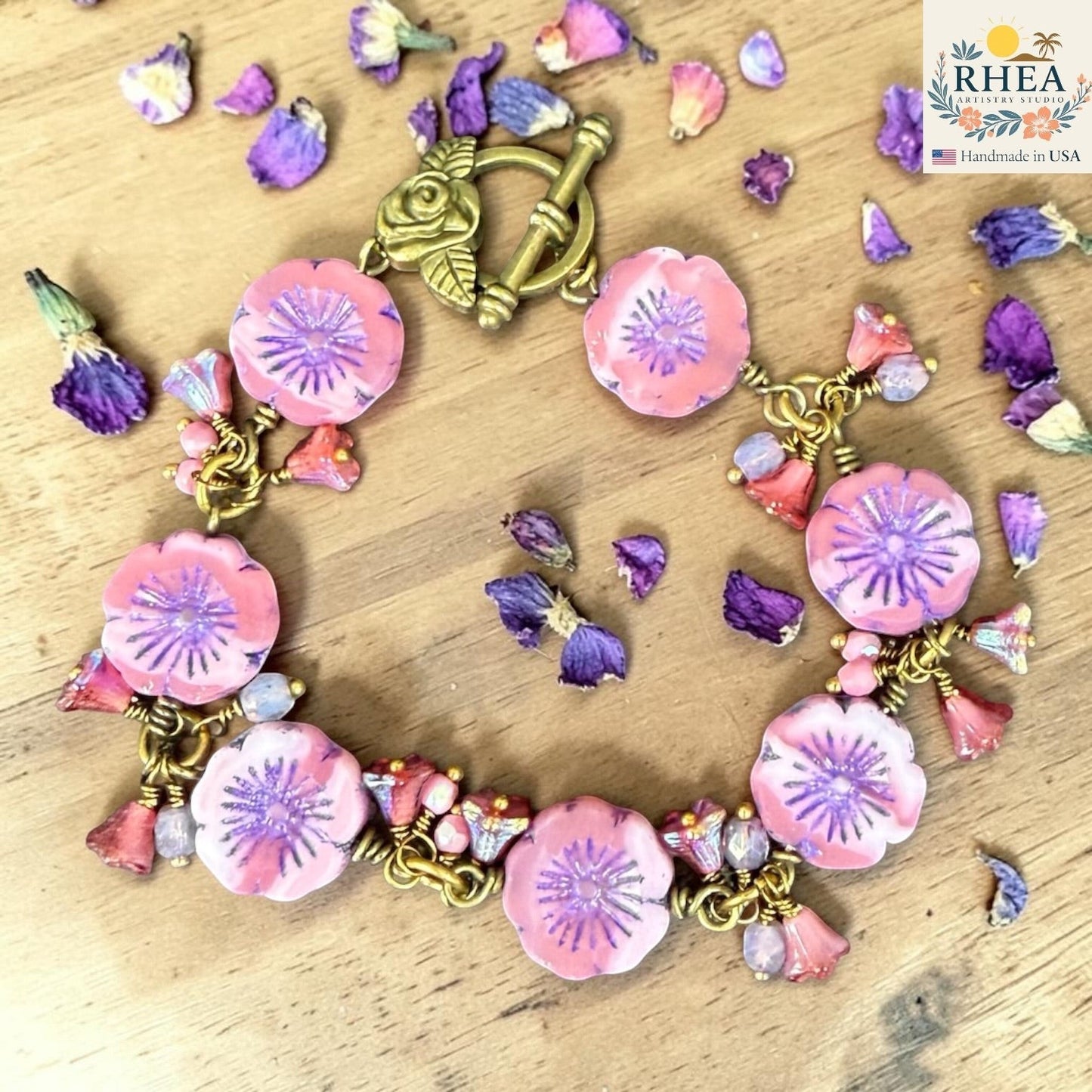 Rhea Artistry Studio handmade bracelet with pink and purple glass flower beads and antique brass toggle clasp, surrounded by dried flowers.