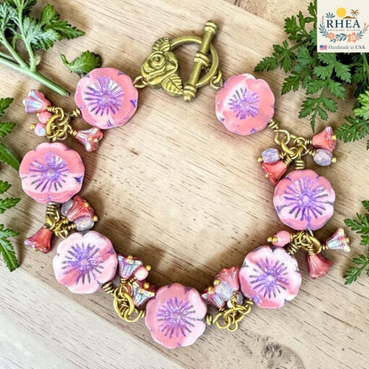 Rhea Artistry Studio handmade bracelet with pink floral glass beads, purple centers, and antique brass toggle clasp with rose detail.
