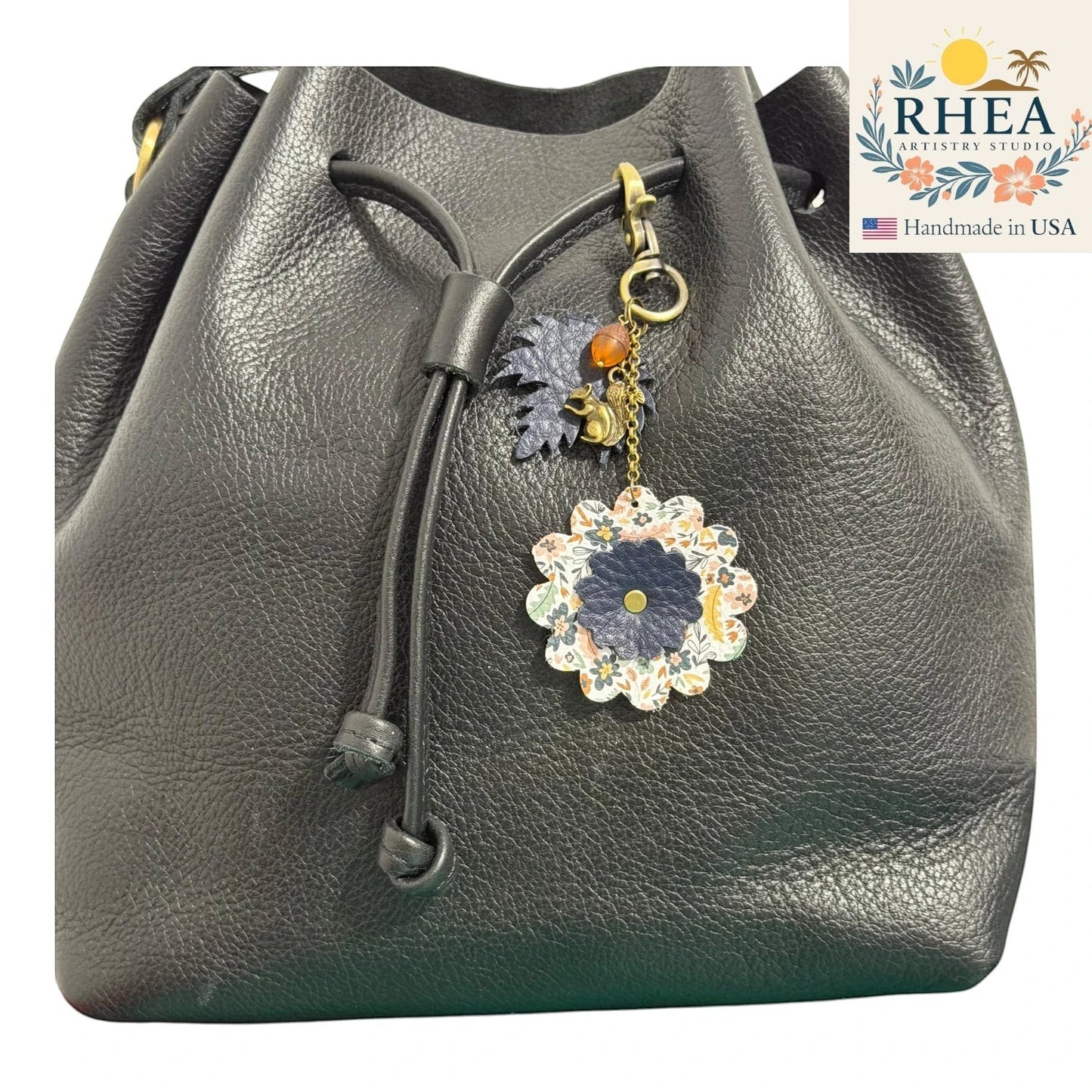 Rhea Artistry Studio black leather drawstring bag with a floral leather charm featuring a squirrel and acorn detail.
