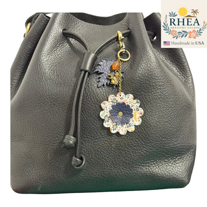 Rhea Artistry Studio black leather drawstring bag with a floral leather charm featuring a squirrel and acorn detail.
