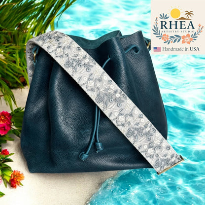 Rhea Artistry Studio 2-inch wide crossbody strap with embroidered frosted flora pattern in grey and white, adjustable length, brushed brass hardware.