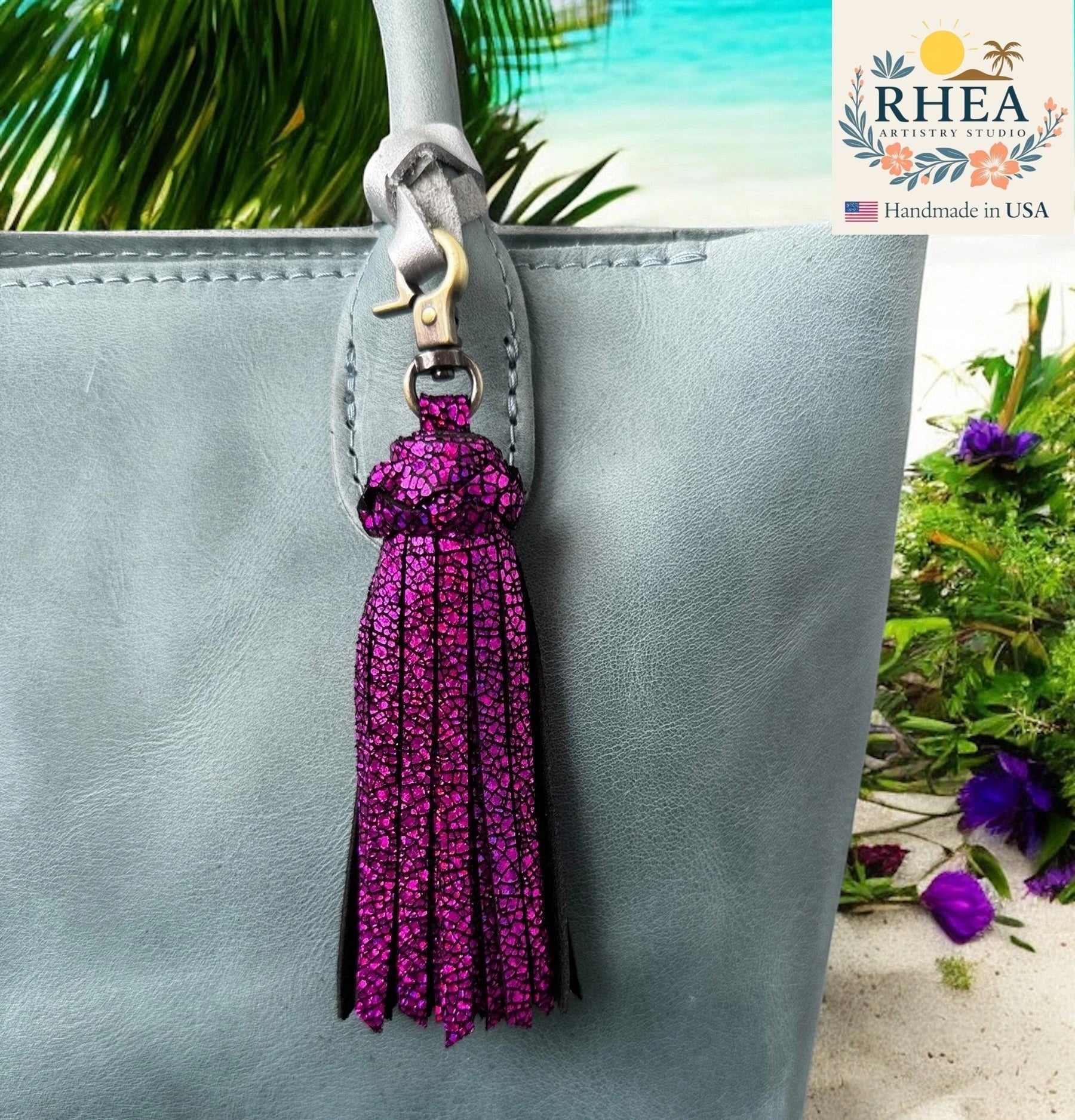 Rhea Artistry Studio handmade large fuchsia glitter leather tassel keychain with lobster clasp attached to a light blue tote bag.