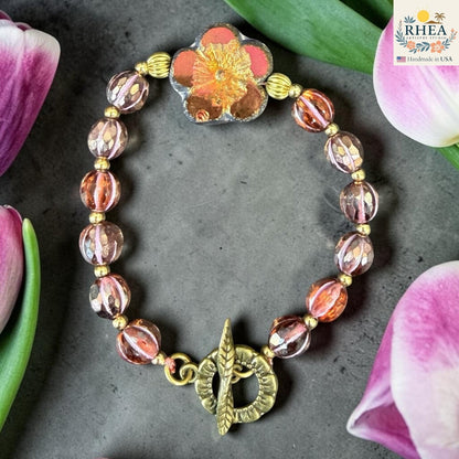 Rhea Artistry Studio handmade garden glass bead bracelet with floral focal element, peach and pink beads, and brass toggle clasp.