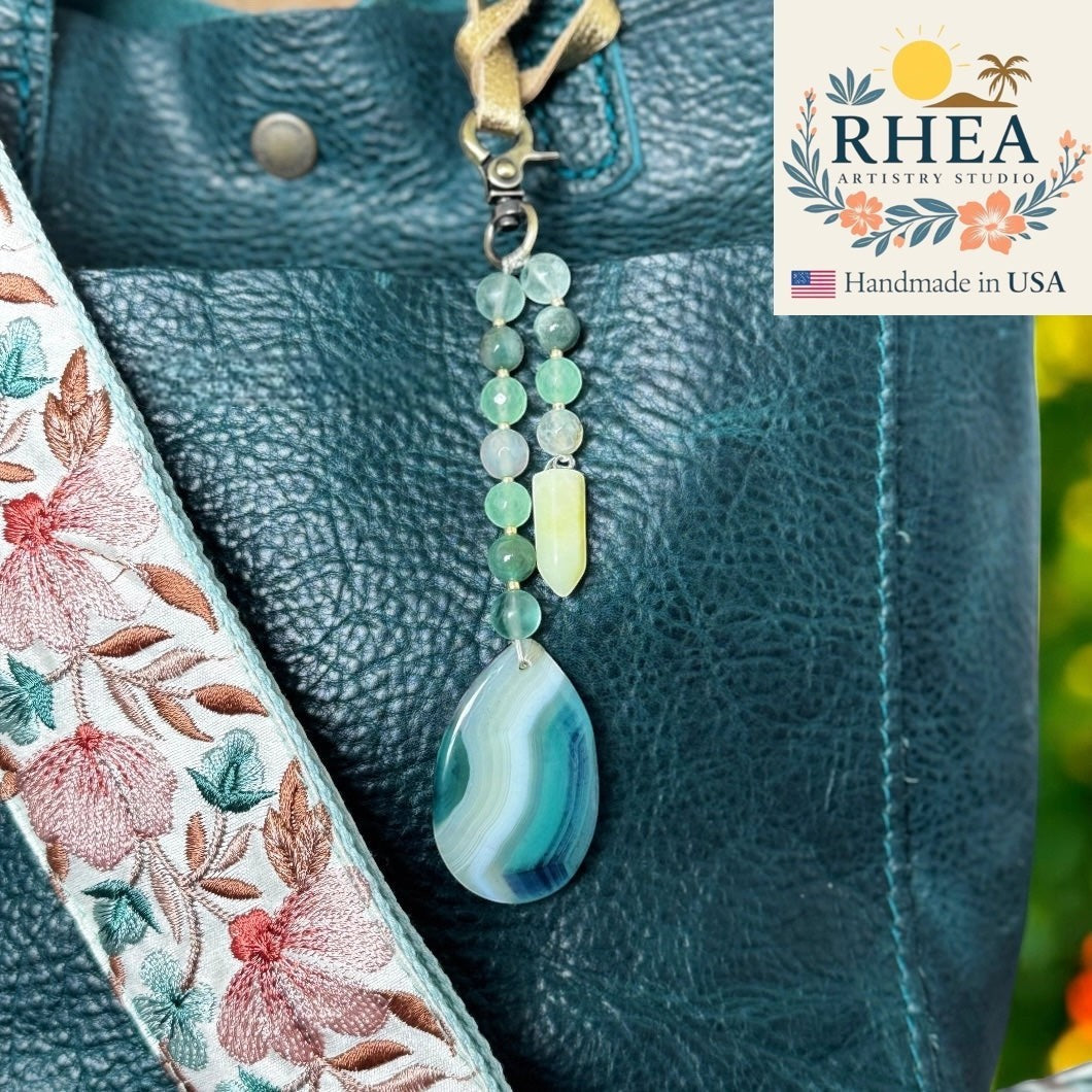 Rhea Artistry Studio double-strand gemstone charm with agate, quartz, and jade in blue and green hues, attached to a teal bag.