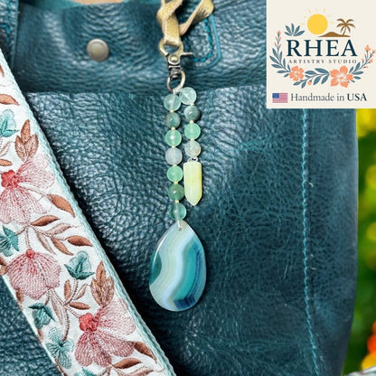Rhea Artistry Studio double-strand gemstone charm with agate, quartz, and jade in blue and green hues, attached to a teal bag.