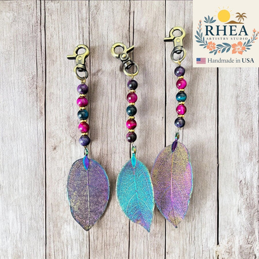 Rhea Artistry Studio handmade bag charm with galaxy gemstone beads and iridescent electroplated leaf pendant, antique bronze clasp.