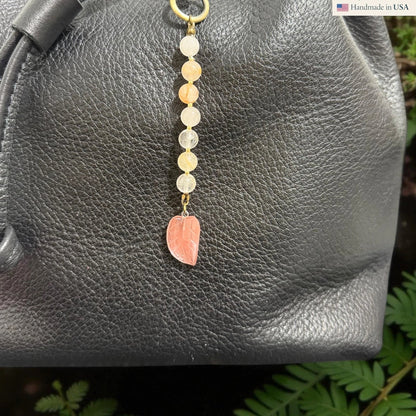 Rhea Artistry Studio handmade gemstone and glass leaf charm with peach and clear beads on a black leather bag.
