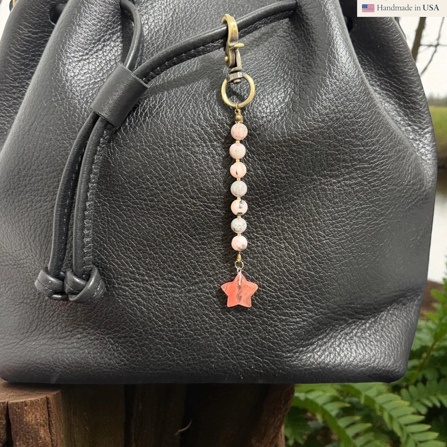 Rhea Artistry Studio handmade pastel pink gemstone and star charm with brass clasp on black leather bag.