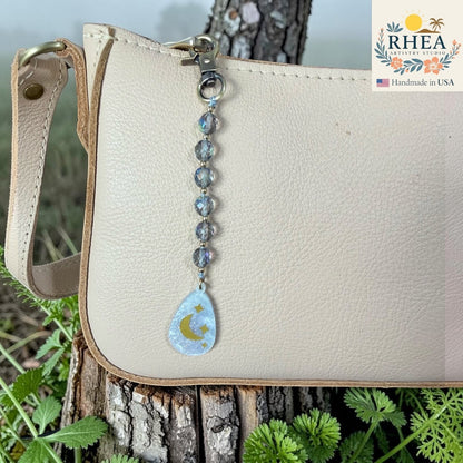 Rhea Artistry Studio handcrafted bag charm with iridescent glass beads and a moon and stars pendant. Brass hardware.