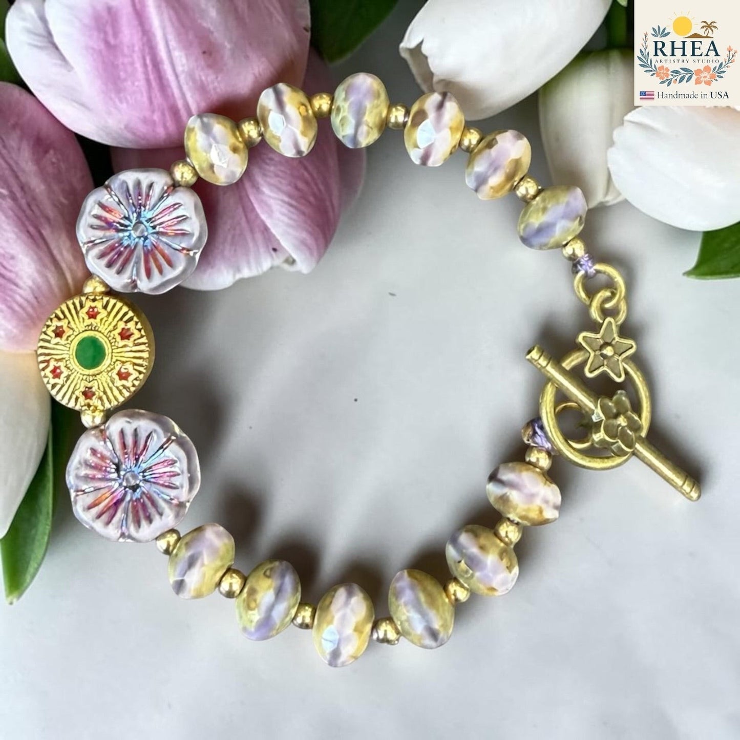 Rhea Artistry Studio handmade glass bead bracelet with floral accents, gold toggle clasp, and pastel yellow and purple beads.