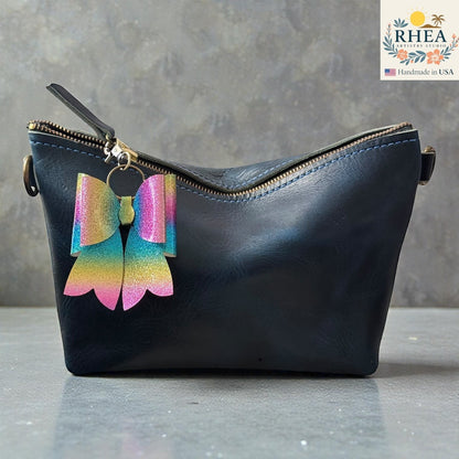 Rhea Artistry Studio handmade glitter bow bag charm with rainbow ombre and brass hardware.