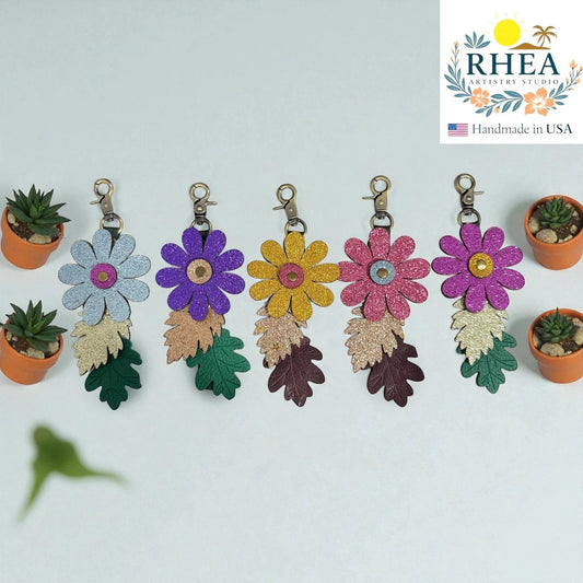 Rhea Artistry Studio glitter leather flower charms with embossed leaves and antique brass clasps. Available in blue, purple, yellow, pink, and magenta.