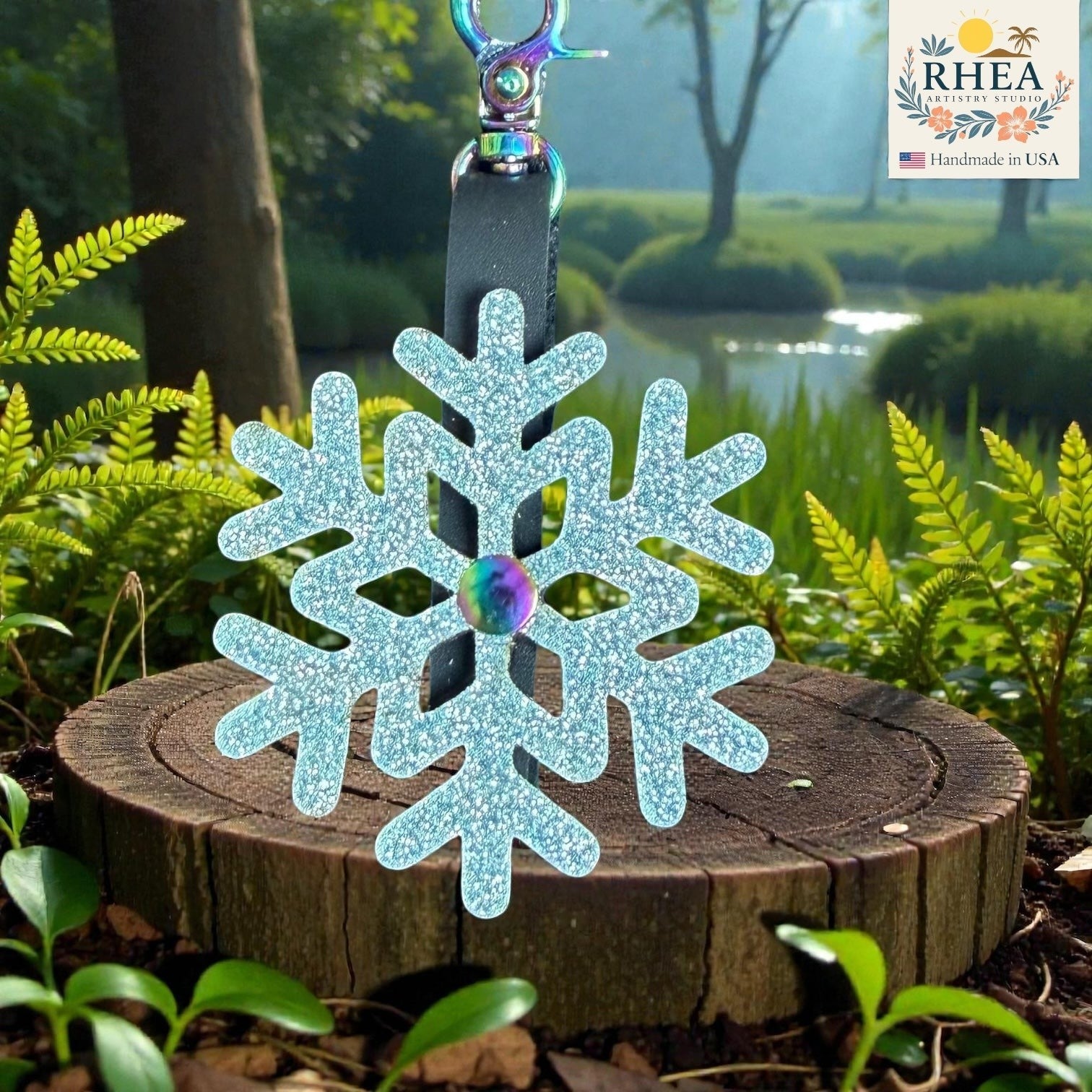 Rhea Artistry Studio light blue glitter snowflake leather charm with rainbow center detail and black strap.