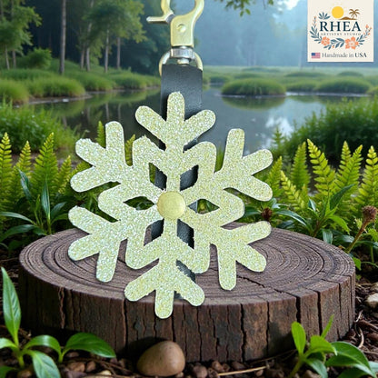 Rhea Artistry Studio light green glitter snowflake leather charm with brass accent, clipped to a black leather strap.