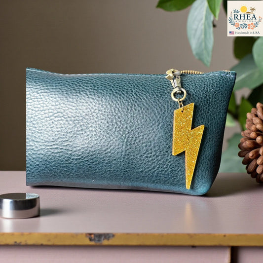 Rhea Artistry Studio gold glitter lightning bolt acrylic charm attached to a teal leather zipper pouch.