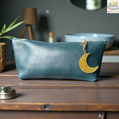 Rhea Artistry Studio gold glitter moon acrylic charm attached to a teal leather pouch zipper.