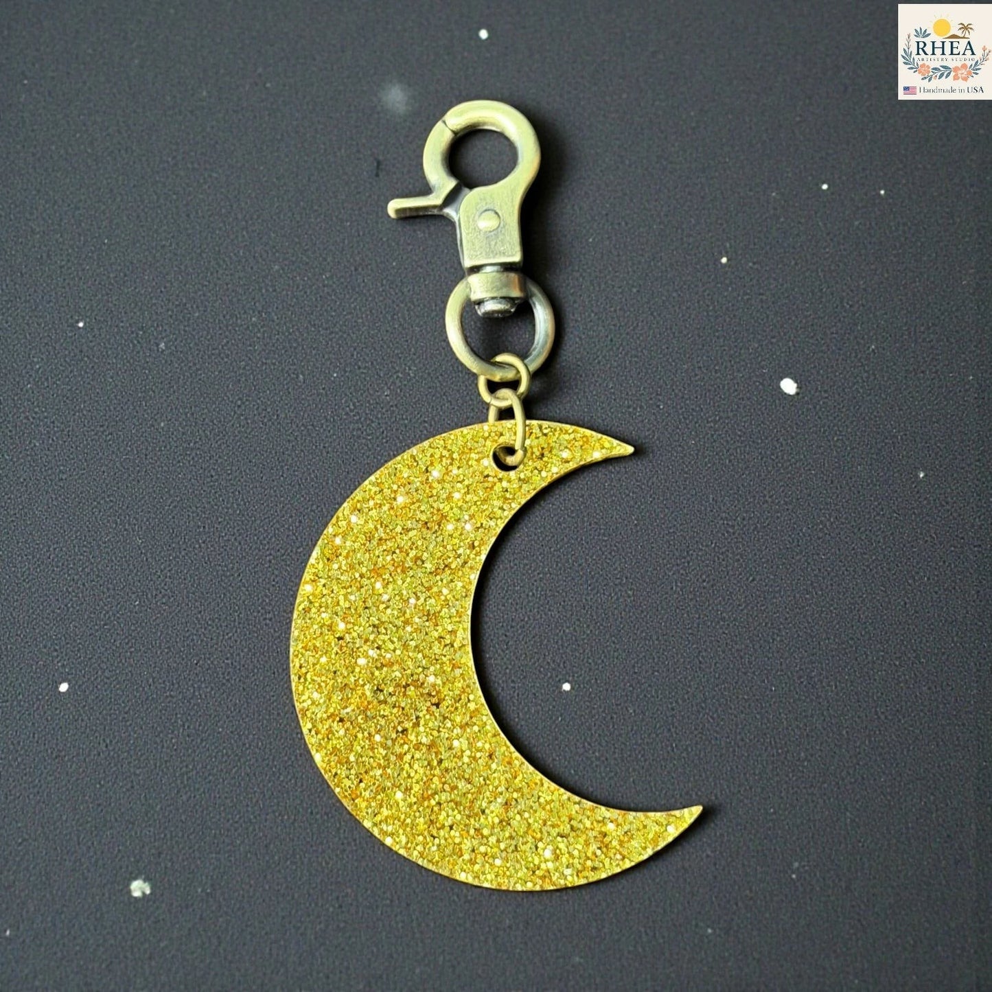 Rhea Artistry Studio gold glitter moon charm with brass clasp, 2 inches long, for bags or zippers.