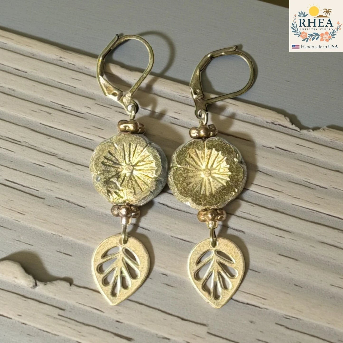 Rhea Artistry Studio handmade gold hibiscus glass drop earrings with leaf charms and lever back hooks.