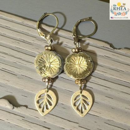 Rhea Artistry Studio handmade gold hibiscus glass drop earrings with leaf charms and lever back hooks.