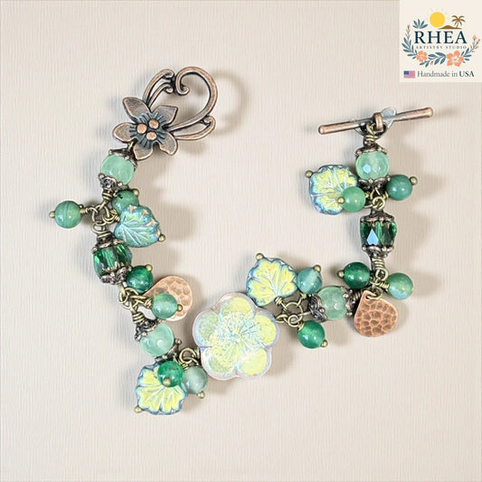 Rhea Artistry Studio handmade bracelet with green agate and glass beads, floral and leaf motifs, and antique-toned toggle clasp.