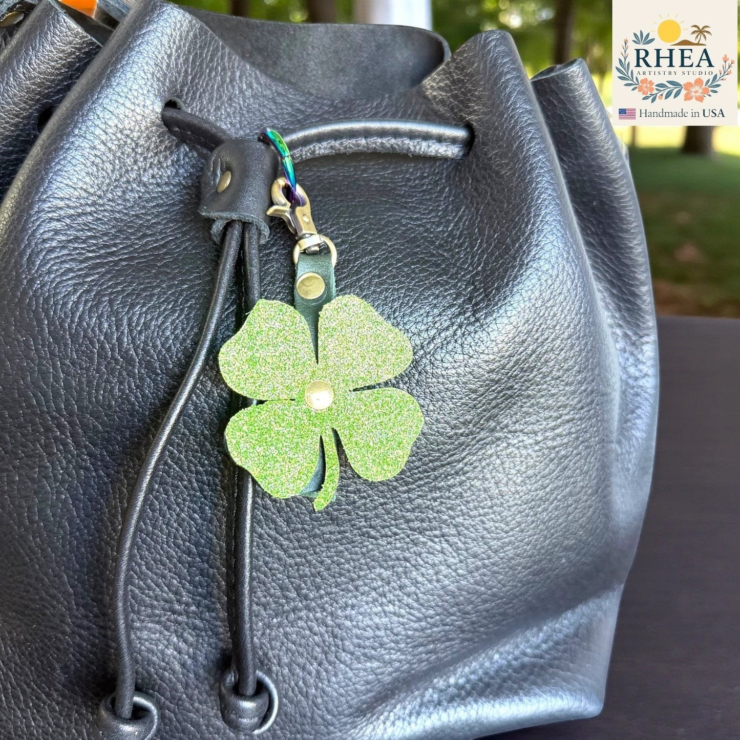Rhea Artistry Studio green glitter leather clover charm with brass hardware attached to a black leather bag.