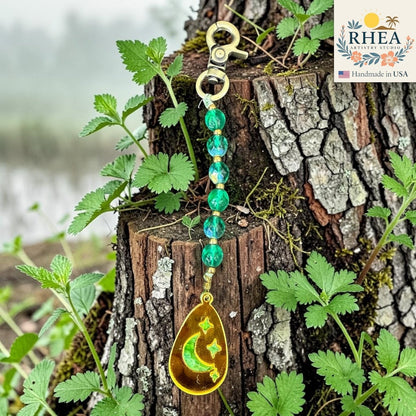Rhea Artistry Studio green multi-faceted glass bead bag charm with engraved moon and stars pendant and brass hardware.
