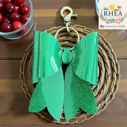 Rhea Artistry Studio handmade green glitter double layer French bow bag charm with brass hardware.