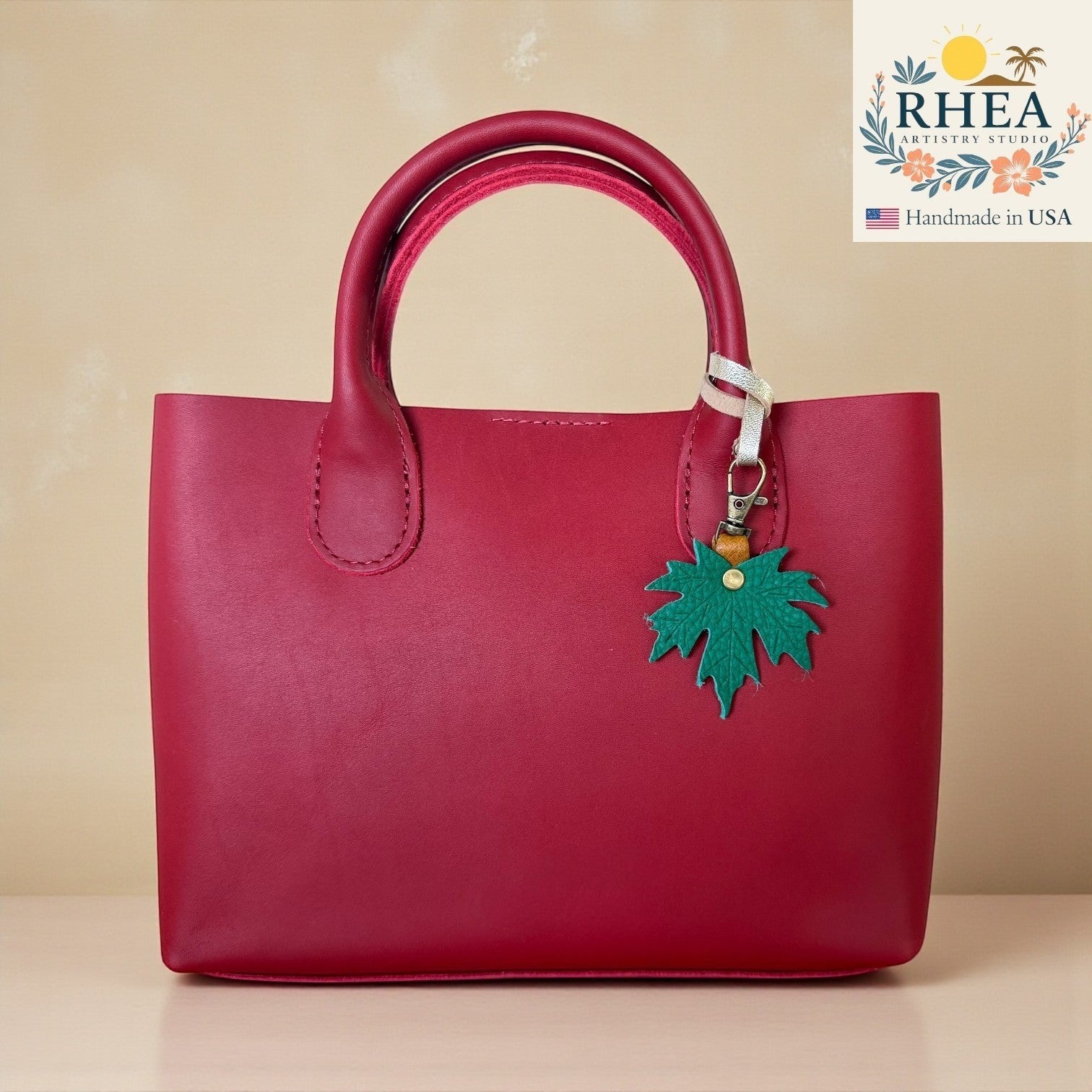 Rhea Artistry Studio green maple leaf charm attached to a red leather handbag.